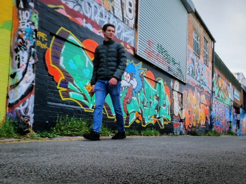 Photograph of Edward Rycroft walking with graffiti in the background in Littlehampton, United Kingdom.